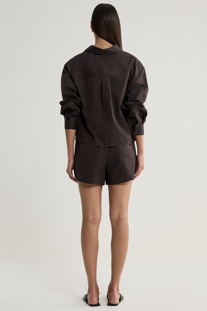 A model viewed from the back wearing a dark brown long-sleeve collared shirt and matching dark brown shorts against a light gray studio background.
