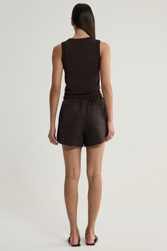 A woman viewed from the back wearing a dark brown sleeveless top and matching dark brown shorts against a light gray studio background.